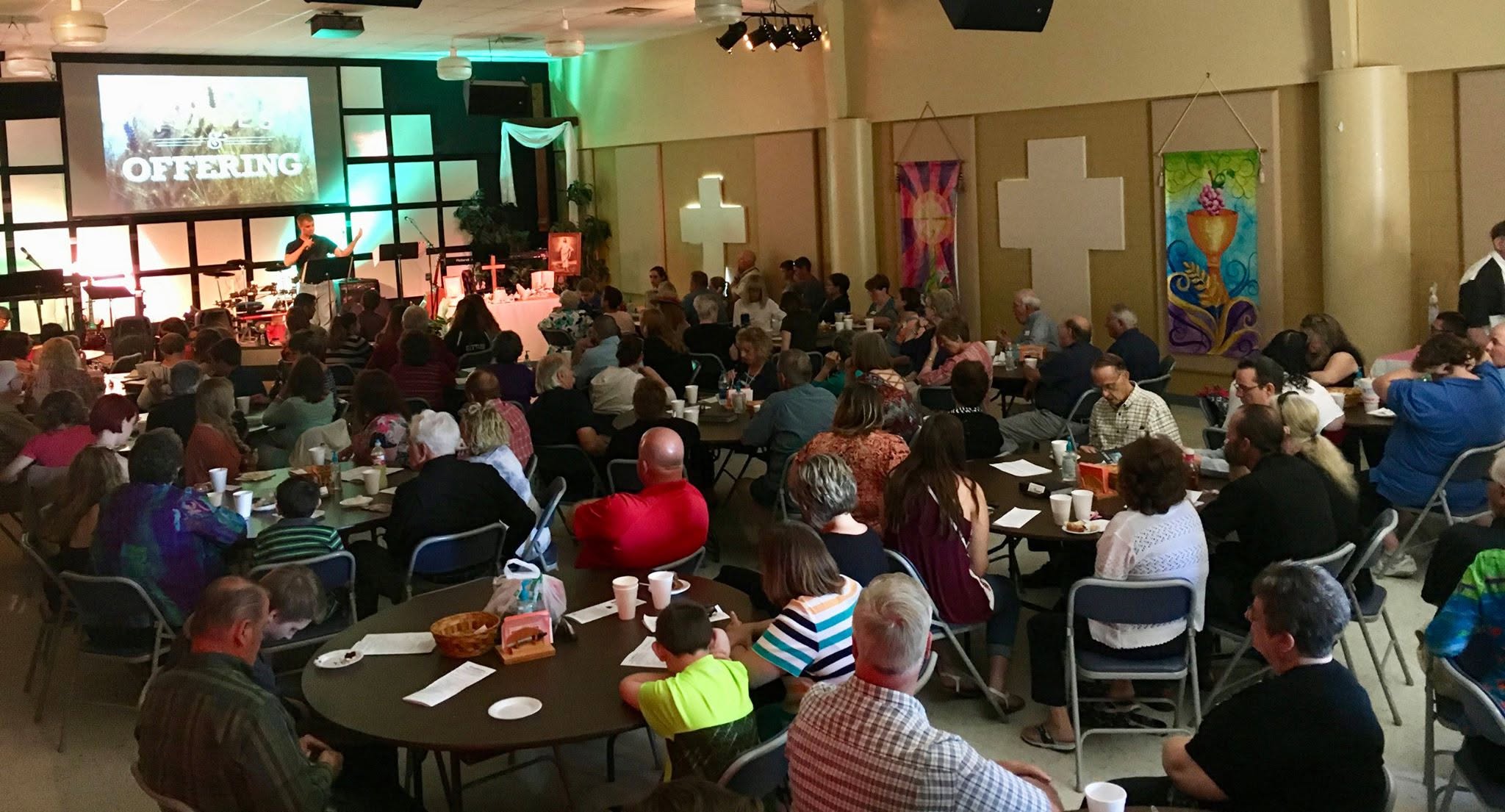 People seated around tables facing the KCMC worship stage